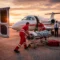 Medical responders load a patient on a stretcher into a small medical evacuation jet on an airport runway, with an ambulance parked nearby at sunset.