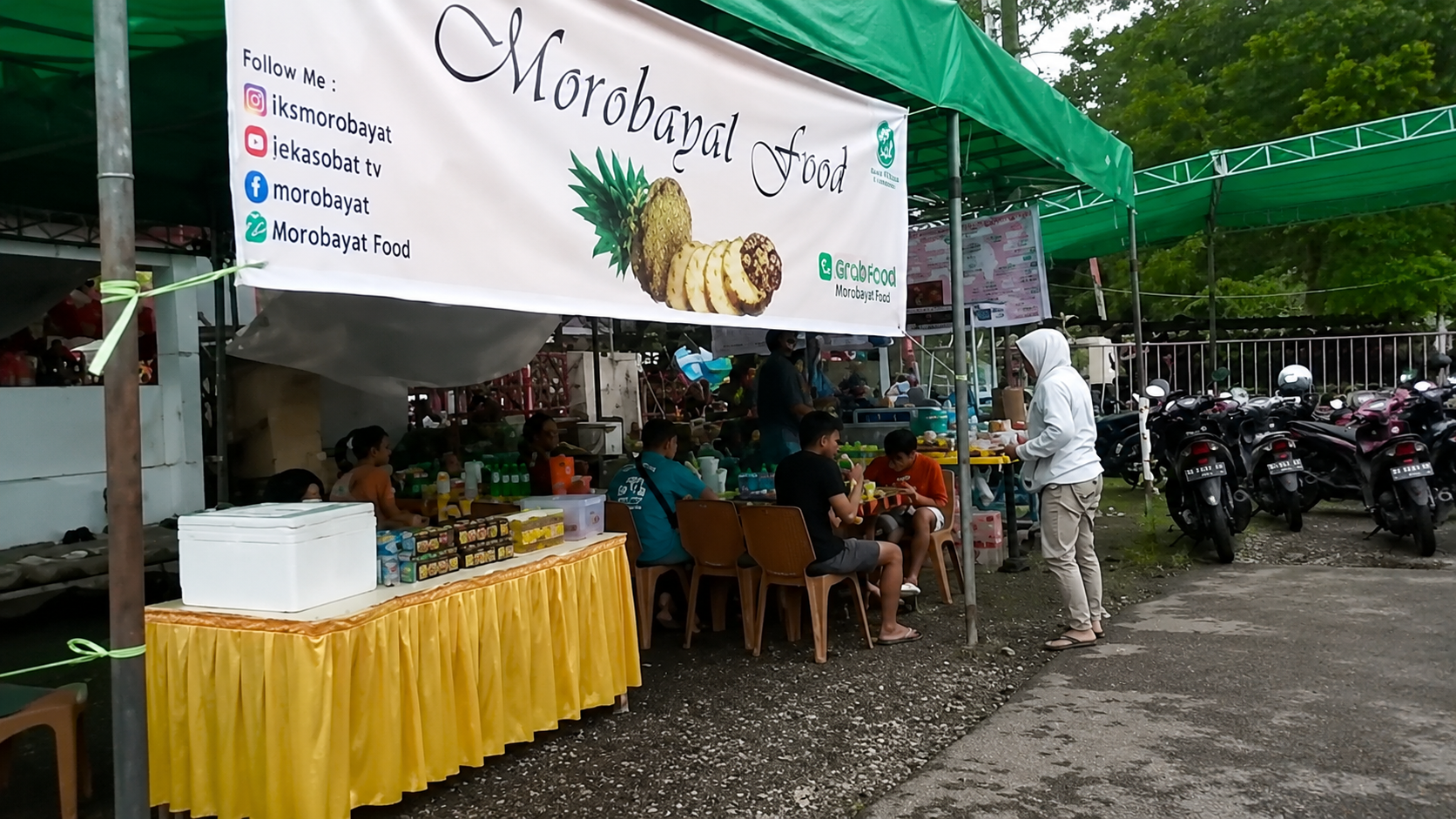 Suasana warung kuliner Morobayat Food di area outdoor dengan pengunjung yang sedang menikmati makanan di bawah tenda hijau
